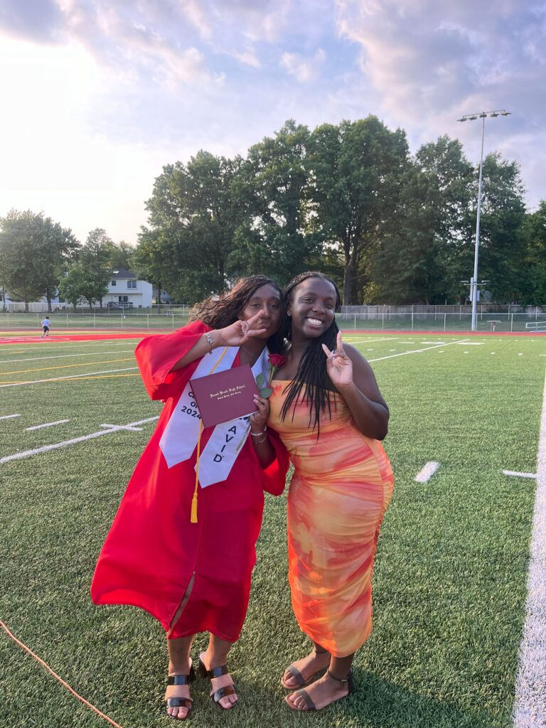 A photo of a graduate posing with a friend with peace signs on the LaMonte Field at graduation.