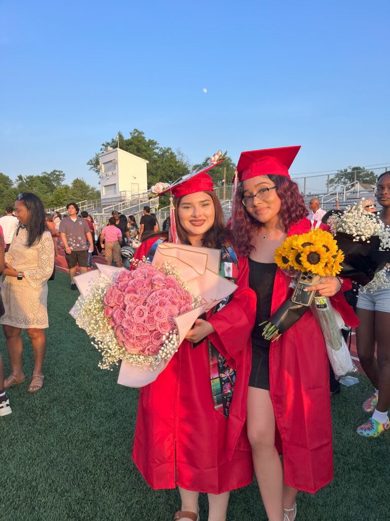 Two graduates smile holding bouquets of flowers after the ceremony.