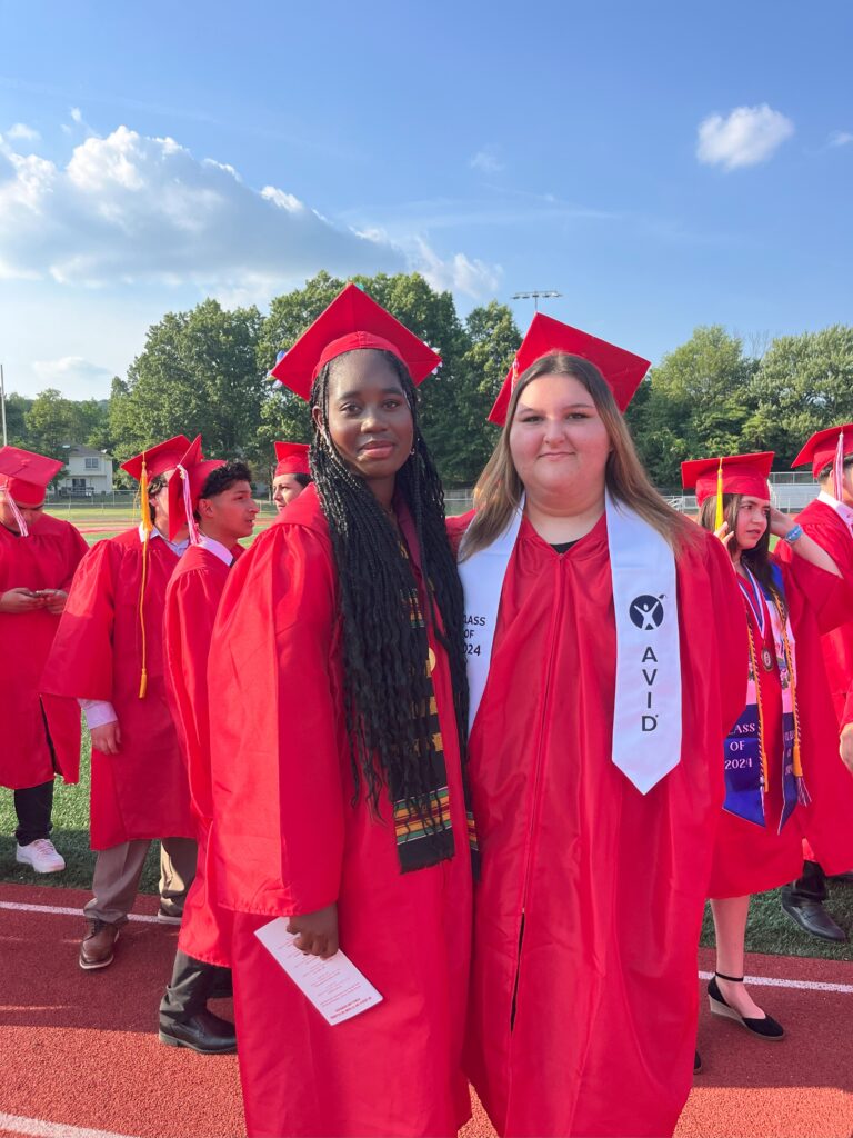 A photo of two graduates before the ceremony in their red cap and gowns.