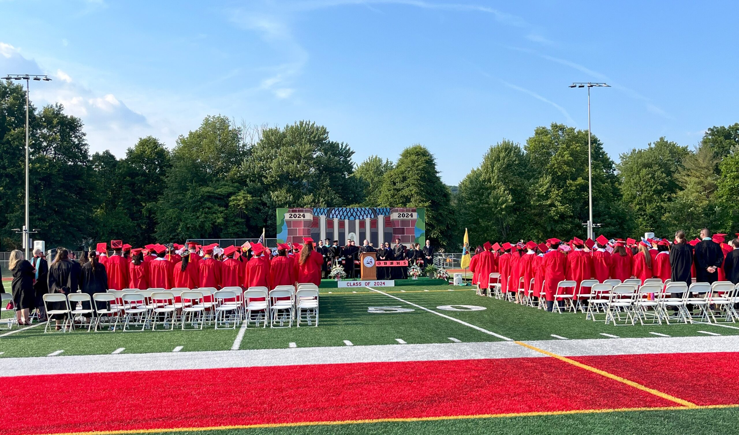 The class of 2024 excitedly sit on the field facing the stage where Principal Edward Smith address the graduates.